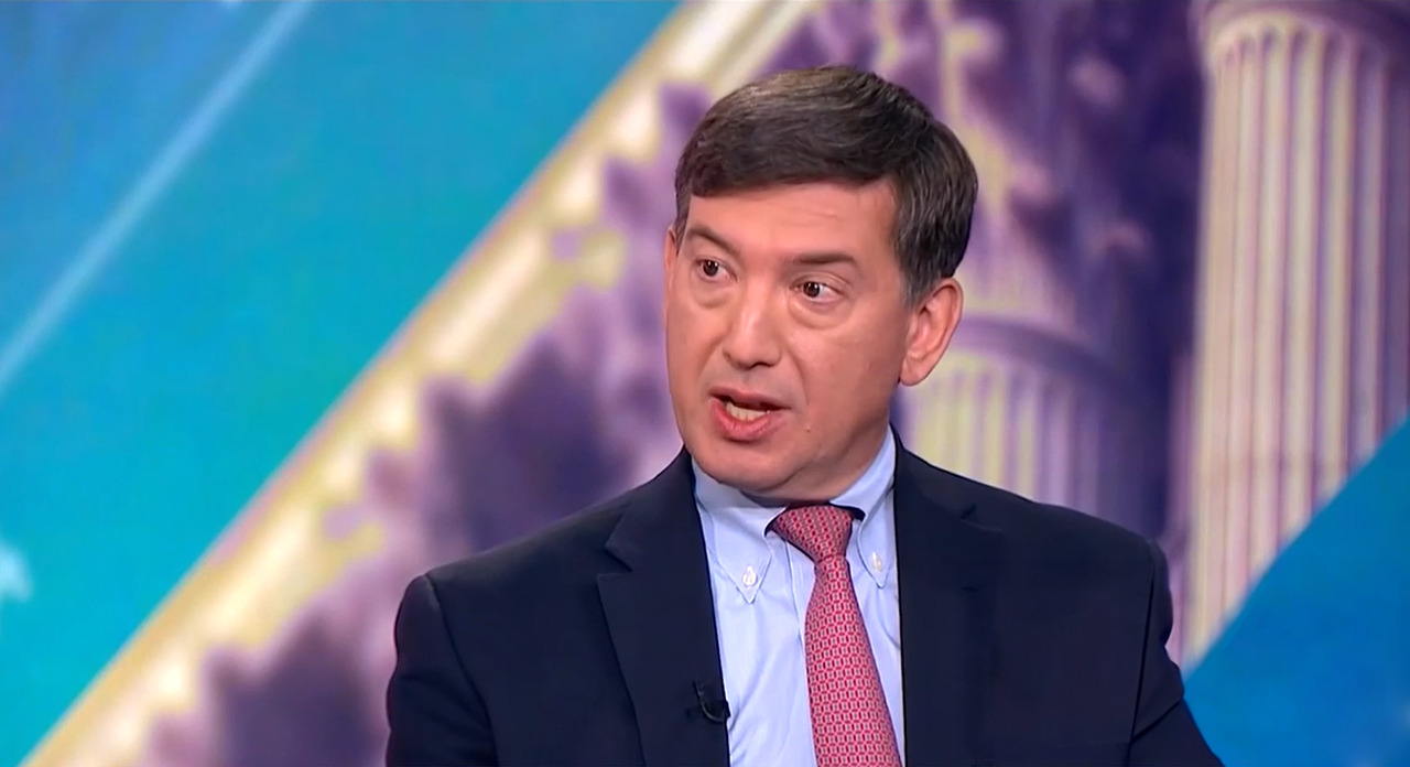 Apollo Co-President Scott Kleinman speaking during a televised interview, discussing private equity strategy against a backdrop featuring architectural columns and a stylized blue and purple gradient.